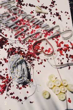 scissors and yarn are laying on a table with red confetti scattered around it