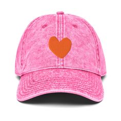 a pink hat with an orange heart embroidered on the front and back side, against a white background