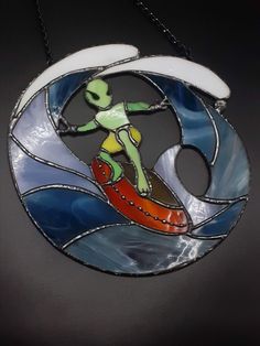 a stained glass ornament depicting a surfer on a wave with an alien figure