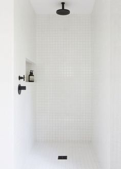 a white tiled shower stall with black fixtures