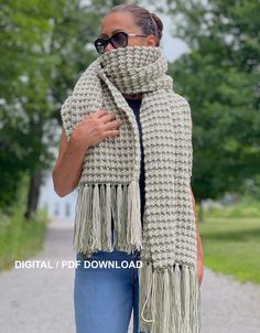 a woman wearing a crochet scarf and sunglasses is standing on a path in the park