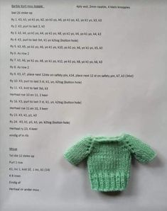 a green knitted sweater sitting on top of a piece of paper with writing underneath it