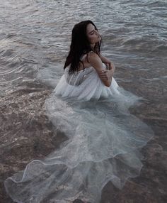 a woman sitting in the water wearing a white dress