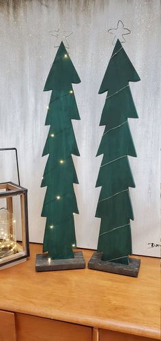 two wooden christmas trees are sitting on a table next to a small clock and lantern