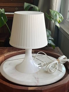 a white lamp sitting on top of a wooden table next to a potted plant