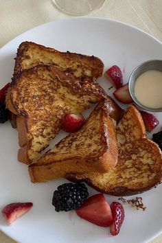 two pieces of french toast on a white plate with berries, strawberries and cream