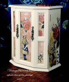 a white cabinet with flowers painted on the front and sides, sitting on top of a wooden table