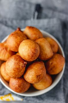 a white bowl filled with fried doughnuts on top of a gray table cloth