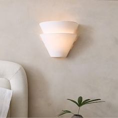 a white wall light mounted on the side of a wall next to a plant in a vase