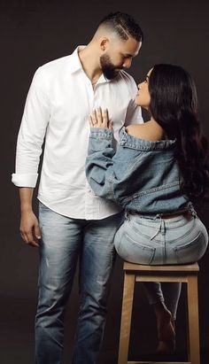 a man standing next to a woman on top of a wooden stool in front of a black background