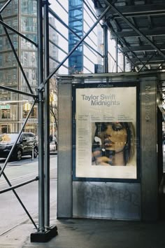 a bus stop with scaffolding around it and a poster on the wall that says taylor swift midnights