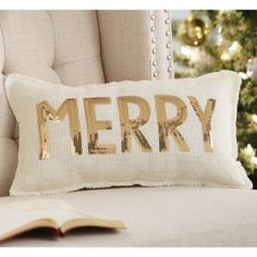 a merry pillow sitting on top of a couch next to a book and christmas tree