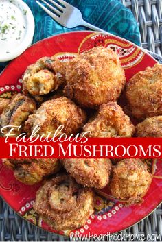 a red plate topped with fried mushrooms next to a bowl of ranch dressing and a fork