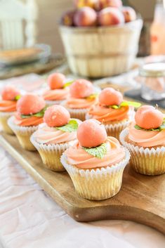 some cupcakes are sitting on a wooden tray with peaches in the background