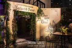 the entrance to an outdoor restaurant at night with greenery on the walls and tables