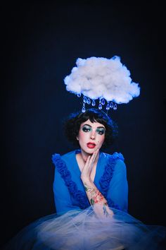 a woman in blue dress with cloud above her head and hands under her chin on black background