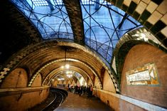 a train station with people standing on the platform and looking up at the skylight