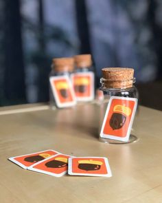 three cards in a glass jar sitting on a table next to two jars with stickers