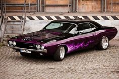 a purple and black muscle car parked in front of a building with graffiti on it