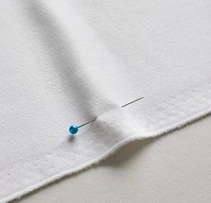 the needle is laying on top of the white fabric with blue pins sticking out of it