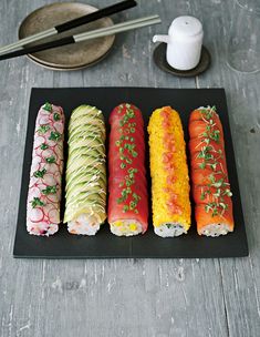 four different types of sushi on a black platter with chopsticks next to it