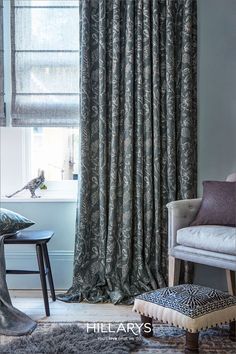 Close up shot of grey curtains with an embroidered floral print. They're layered on top of voile Roman blinds in a light grey. Next to the window, there's a grey chair and an upholstered footstool. Handmade Curtains, Handmade Lampshades, Timeless Interior, Timeless Interiors, Custom Made Curtains, Prestigious Textiles, Grey Curtains, Small Table Lamp, Table Lamp Shades