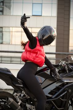 a woman in black tights and a red jacket on a motorbike wearing a helmet