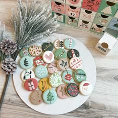 decorated cookies are on a plate next to a pine cone and box of holiday treats