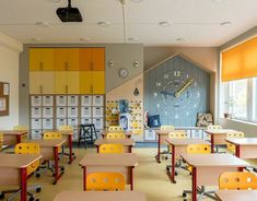 an empty classroom with desks and yellow chairs in front of a large clock on the wall