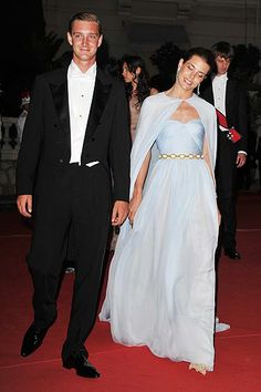 a man and woman dressed in formal wear walking down a red carpeted area at an event