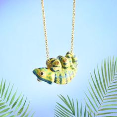 two yellow and blue fish shaped necklaces hanging from a gold chain on a palm tree branch