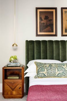 a bed with green velvet headboard and two pictures on the wall next to it