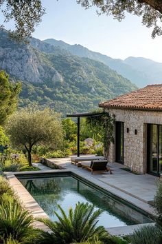 an outdoor swimming pool surrounded by greenery and mountains in the background, with a stone building to the side