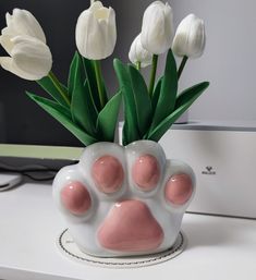 a white vase with pink paws and tulips in front of a computer monitor