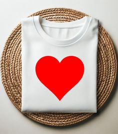 a white t - shirt with a red heart on it sitting on a woven place mat