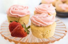 some cupcakes with pink frosting and strawberries on a glass plate next to each other