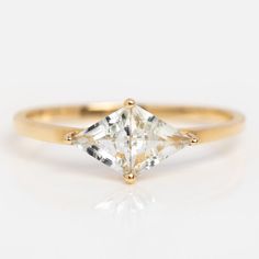 a yellow gold ring with a princess cut diamond in the center, on a white background