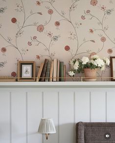 a shelf with flowers and books on it in front of a wallpapered wall