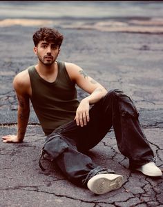 a man sitting on the ground with his legs crossed, wearing jeans and a tank top