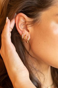 a close up of a person wearing gold ear rings and earrings with one hand on the other side of her ear