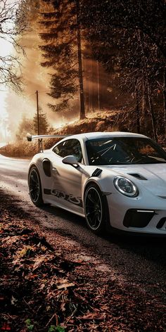 a white sports car driving down a road in the woods with fog and trees around it