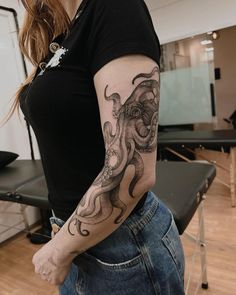 a woman with a tattoo on her arm is standing in front of a chair and looking at the camera