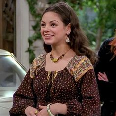 two women standing next to each other in front of a car and one woman is smiling at the camera