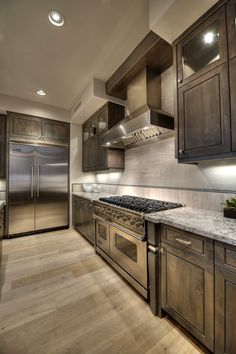 a large kitchen with stainless steel appliances and wood flooring, along with wooden cabinets