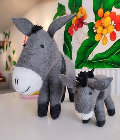 two stuffed donkeys standing next to each other on a white table with colorful wallpaper in the background