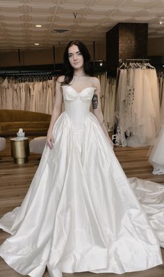 a woman in a white wedding dress standing next to a rack of dresses