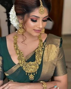 a woman in a green and gold saree with jewelry on her neck, wearing an intricate