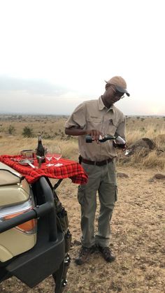 a man standing next to a parked car in the middle of a dry grass field