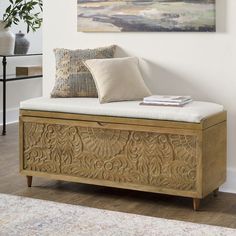 a wooden bench with pillows on it in front of a wall mounted painting and rug