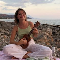 a woman sitting on the beach playing an ukulele